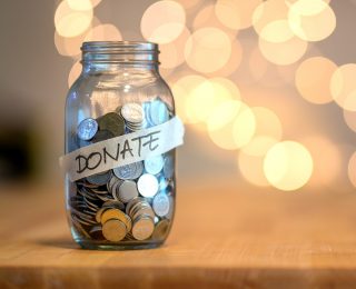 Jar full of coins for donation on wooden desk with blurred background